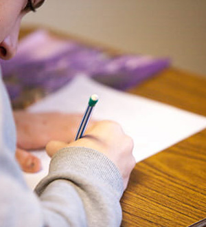 A student writing on a piece of paper with a pencil