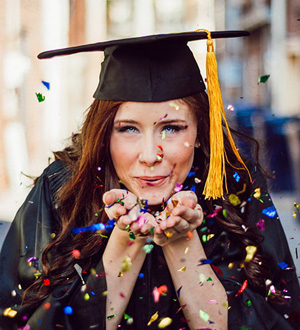 A graduate blowing confetti into the camera